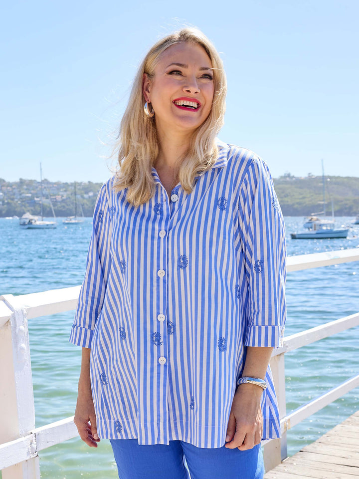 a woman wearing a blue and white striped button-up collared cotton shirt with small embroidered paisley details