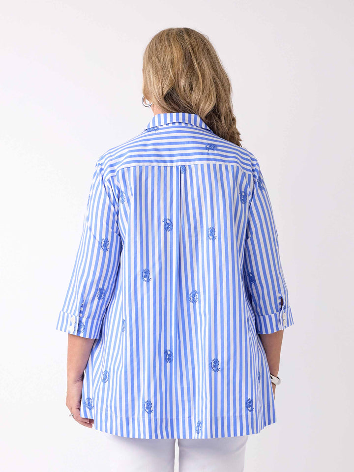 a back view of a woman wearing a blue and white striped button-up collared cotton shirt with small embroidered paisley details