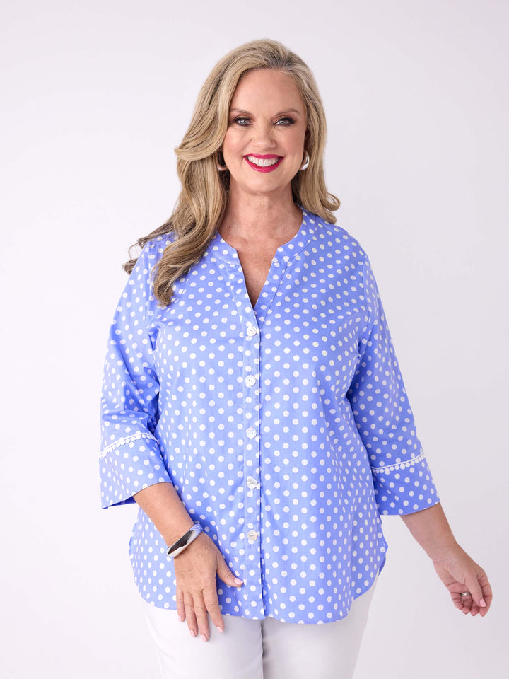 A woman wearing a light blue button-front blouse with white polka dots and white pants