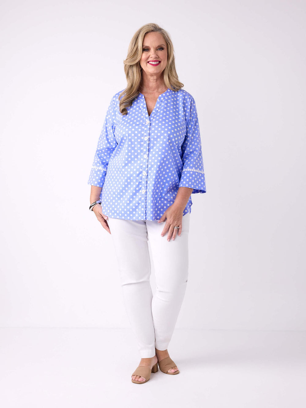 A woman wearing a light blue button-front blouse with white polka dots and white pants