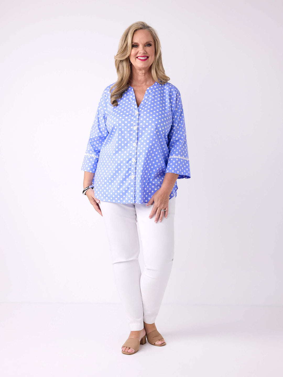 A woman wearing a light blue button-front blouse with white polka dots and white pants