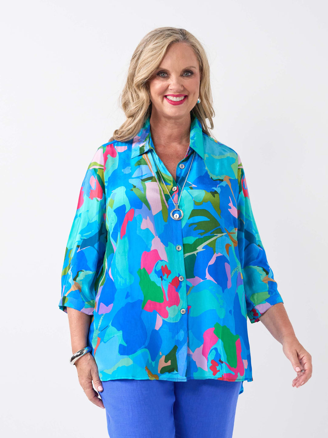A woman wearing a vibrant multicolour printed collared shirt in different shades of blue, paired with cobalt linen pant