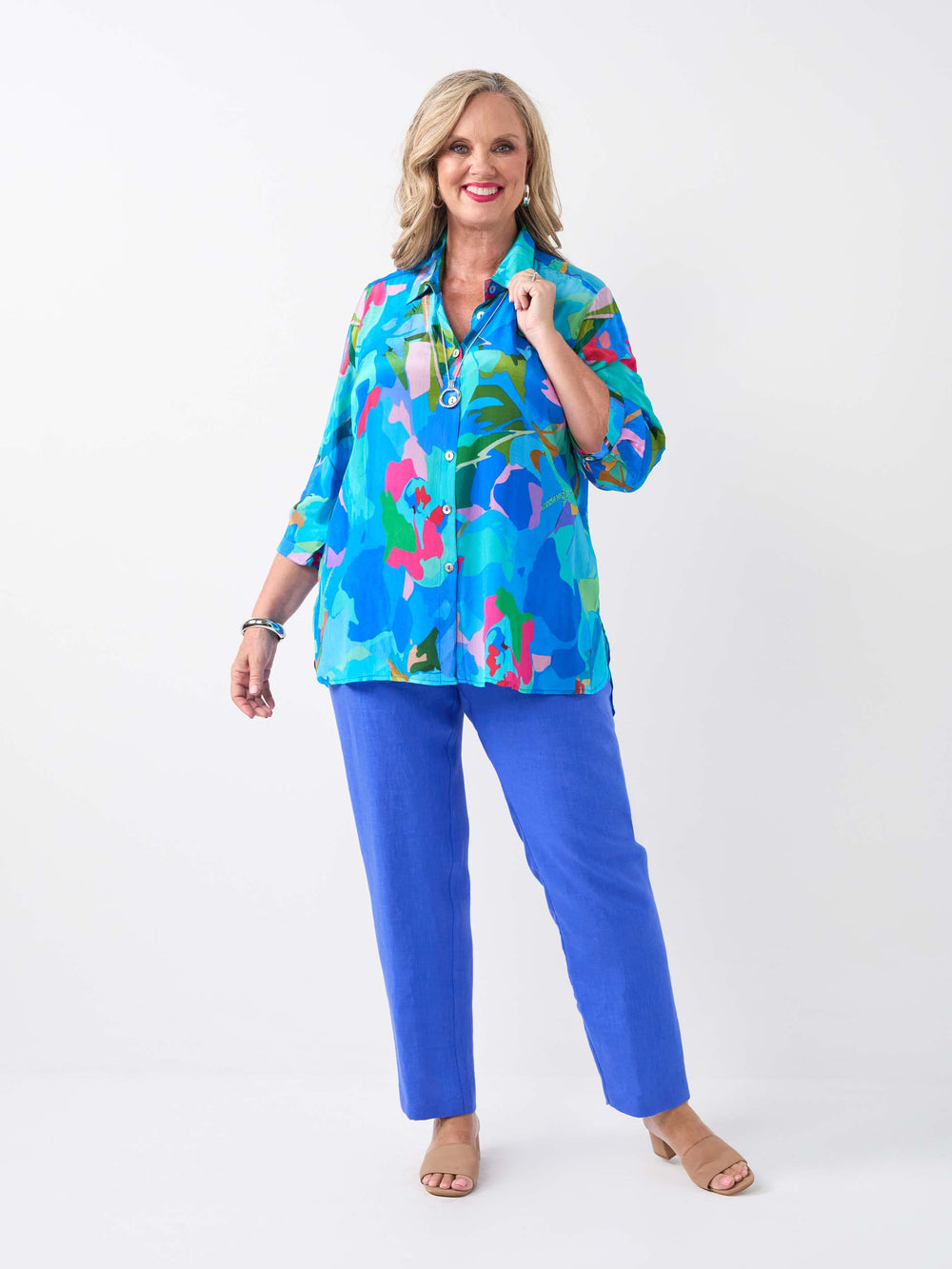 A woman wearing a vibrant multicolour printed collared shirt in different shades of blue, paired with cobalt linen pant