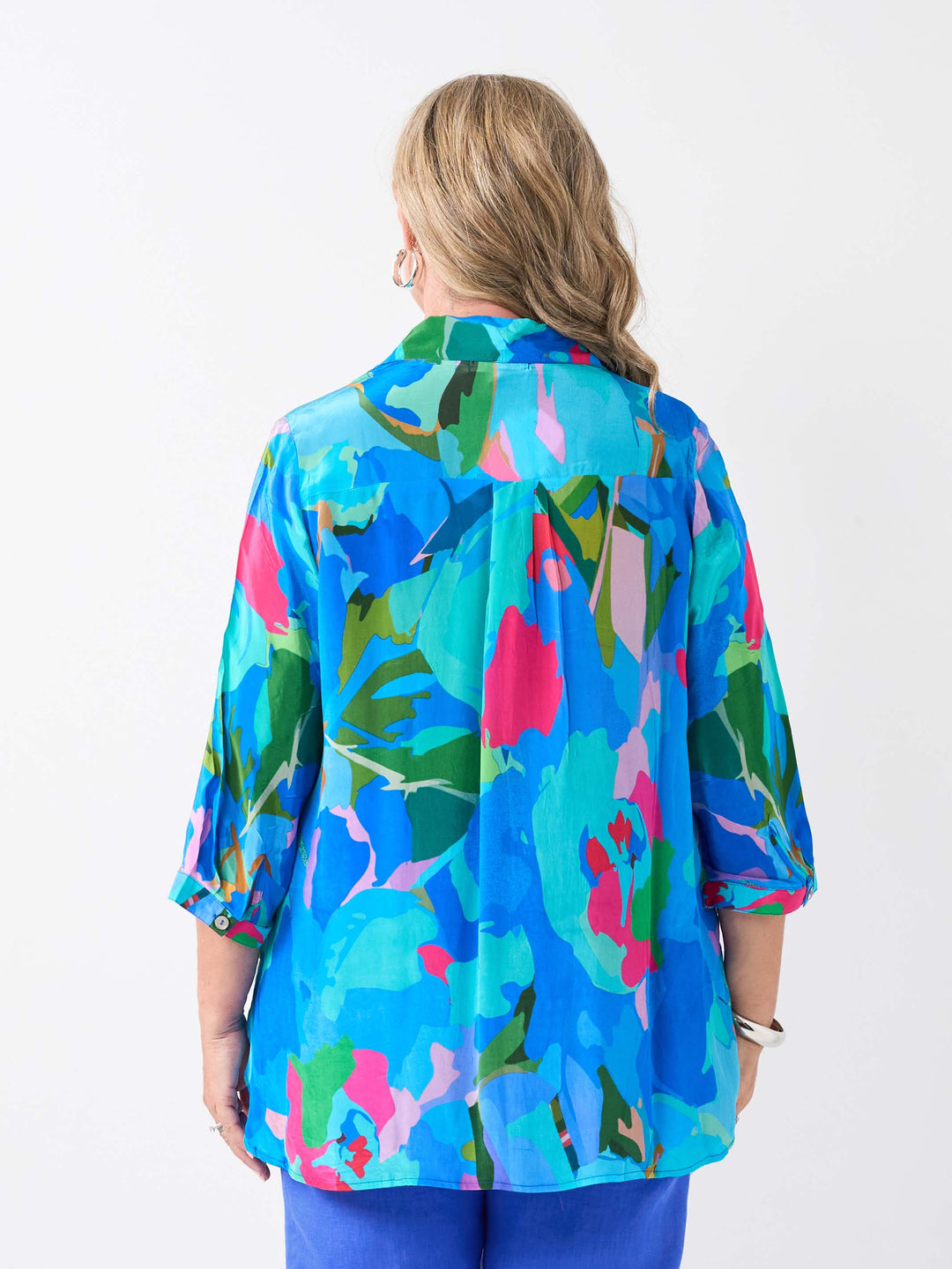 A woman viewed from the back wearing a vibrant multicolour printed collared shirt in different shades of blue, paired with cobalt linen pant