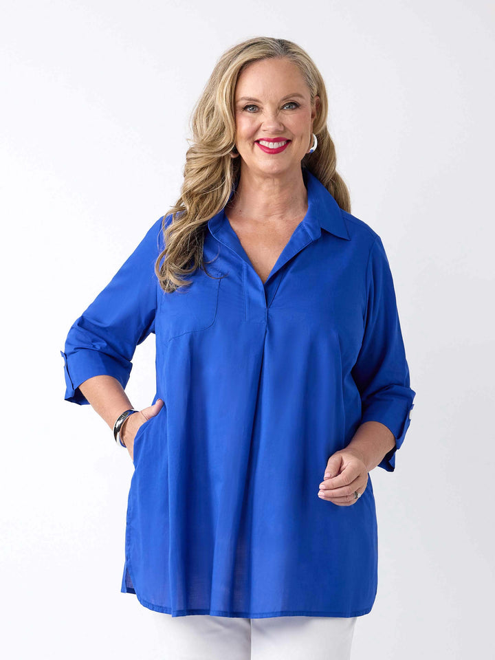 front view of model wearing a bright royal blue collared cotton top with three-quarter tab sleeves and white pants