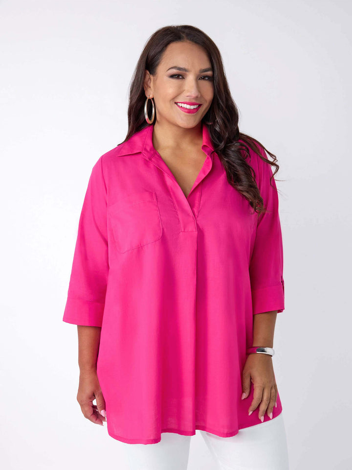 model wearing a bright pink collared top with three-quarter sleeves, paired with white pants