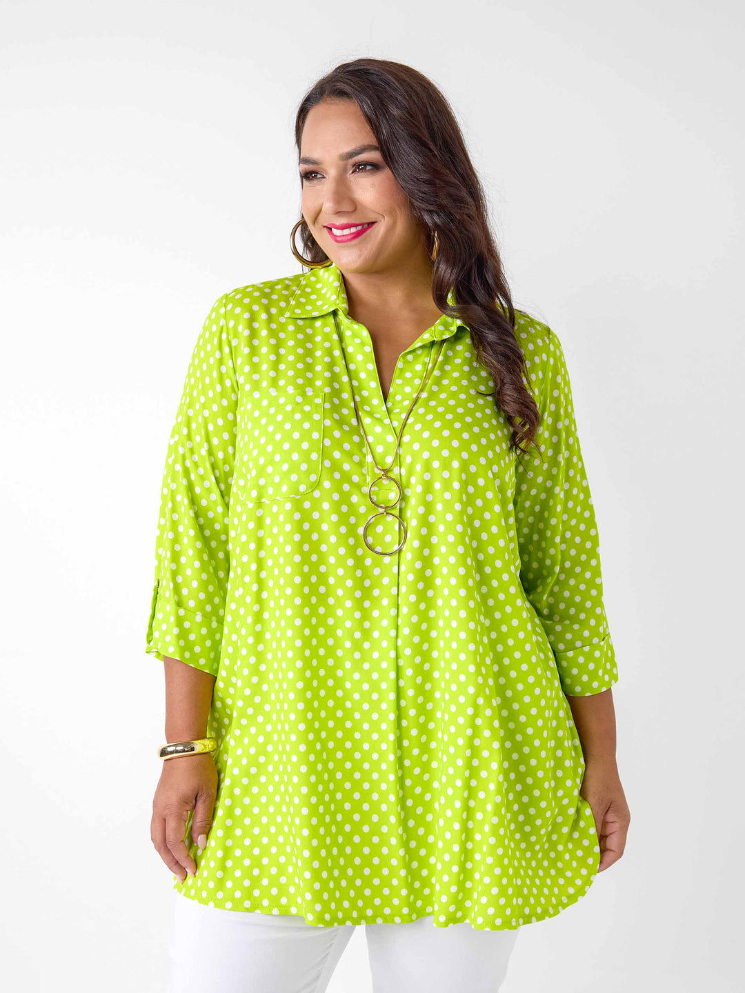 A woman wearing a bright lime green collared top with a white polka dot, paired with white pants