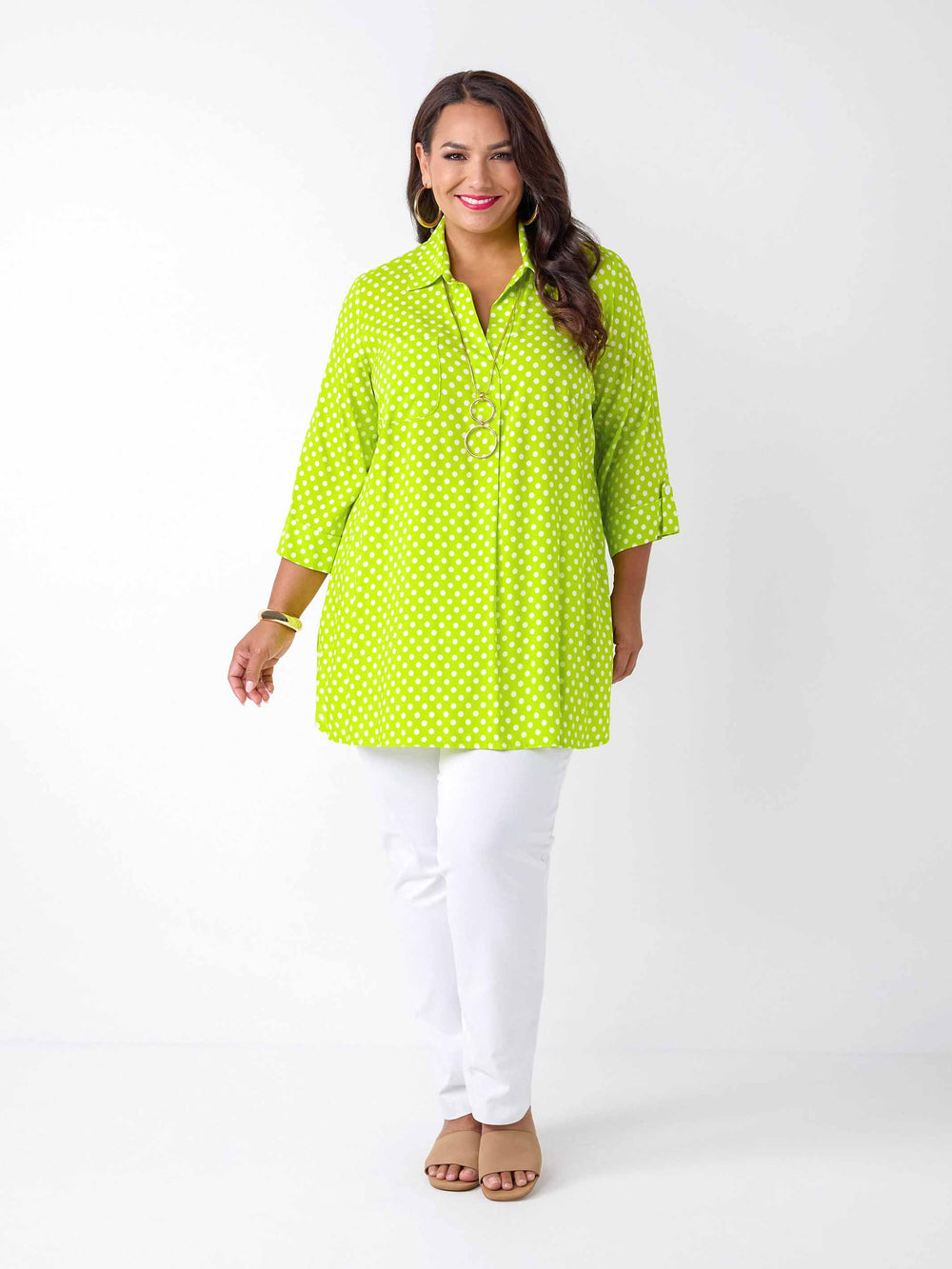 A woman wearing a bright lime green collared top with white polka dots, paired with white pants 