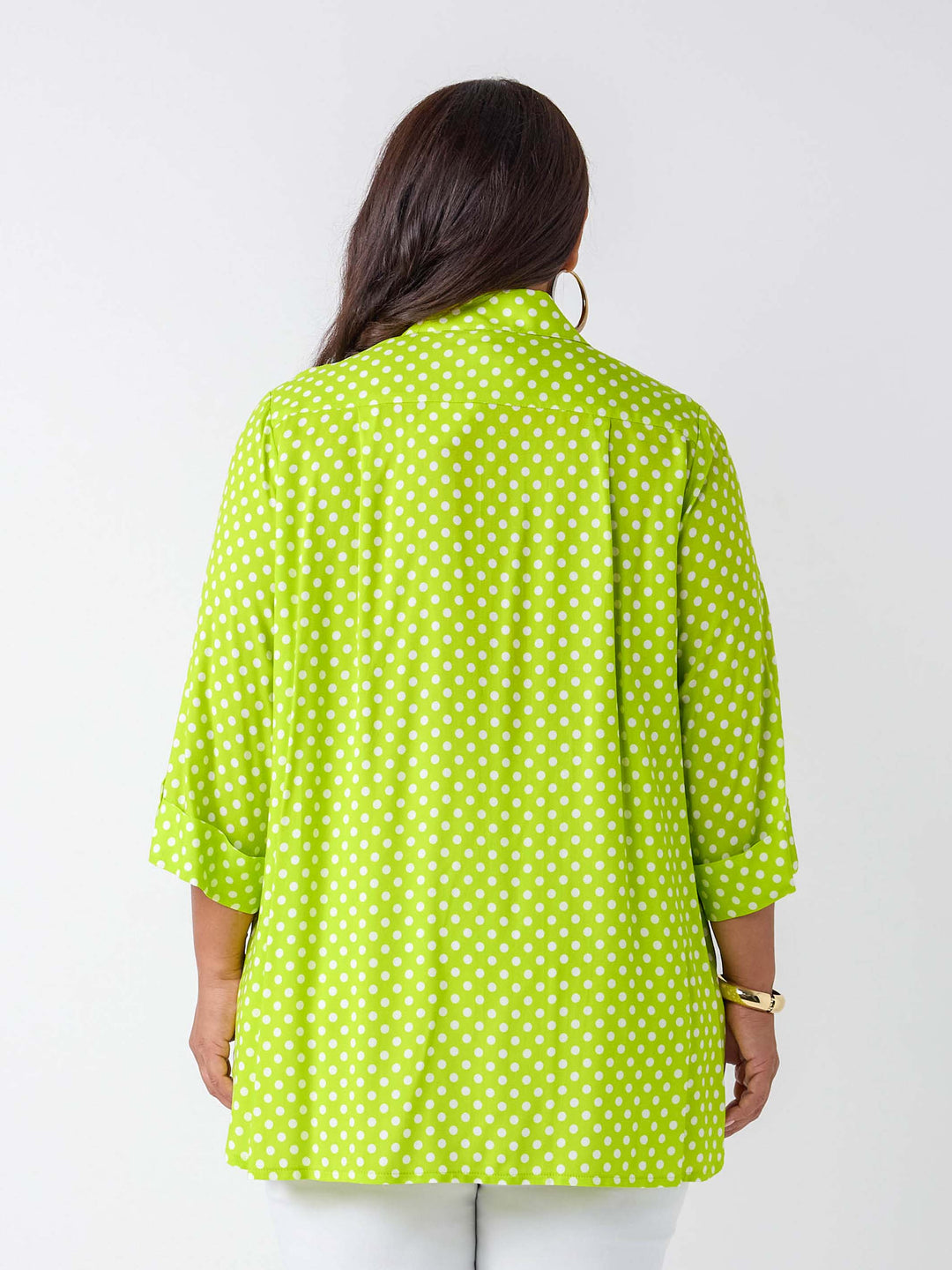 A woman viewed from the back wearing a bright lime green and white polka dot shirt with three-quarter sleeves, paired with white pants