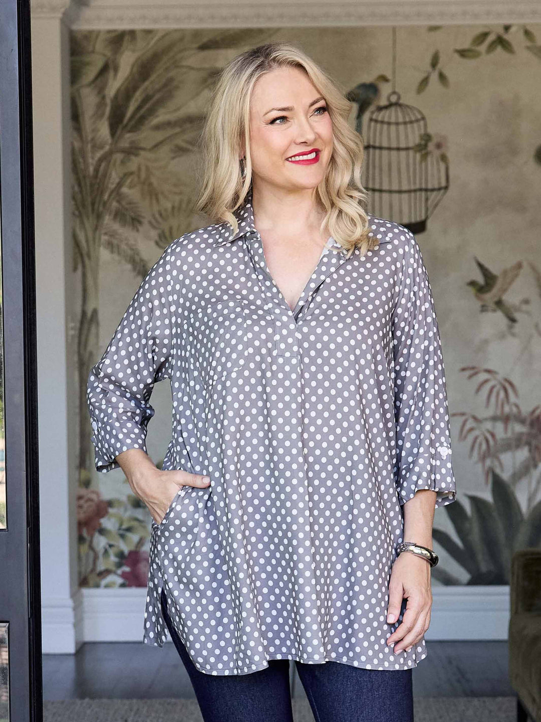 A woman wearing a grey and white polka dot collared top with three-quarter sleeves, paired with dark blue jeans