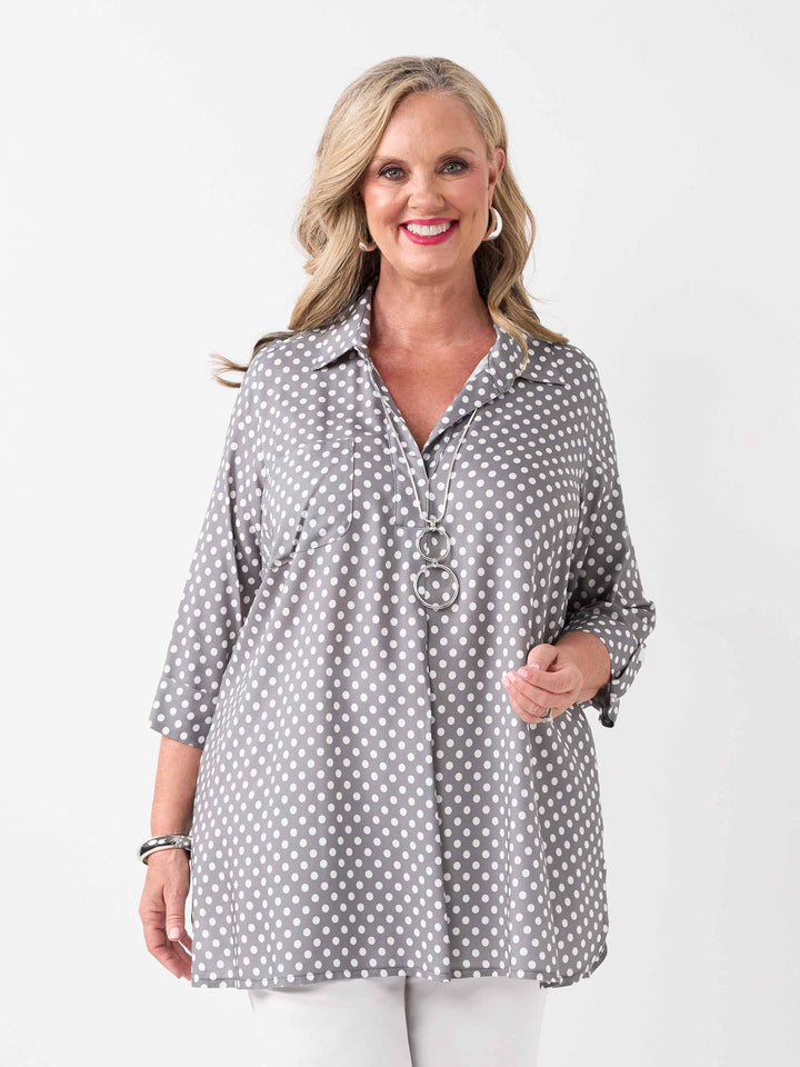 A woman wearing a grey and white polka dot collared top with three-quarter sleeves, paired with white pant