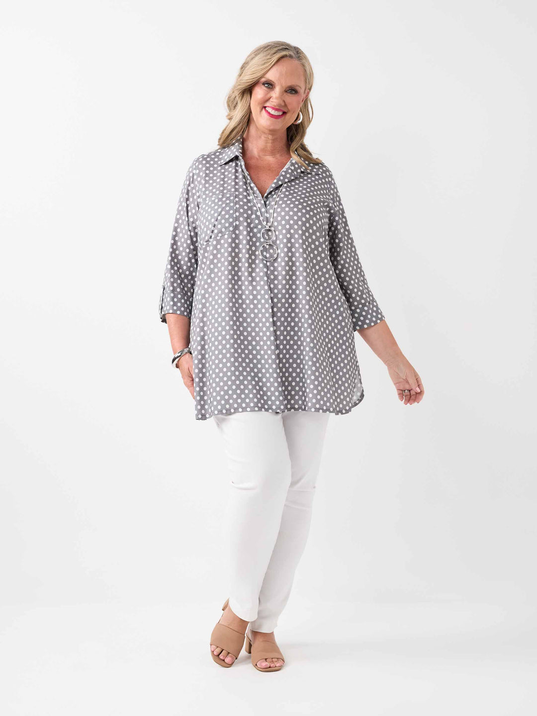 A woman wearing a grey and white polka dot collared top with three-quarter sleeves, paired with white pant