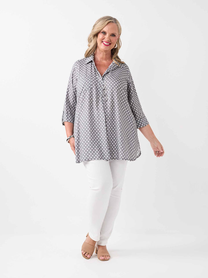 A woman wearing a grey and white polka dot collared top with three-quarter sleeves, paired with white pant
