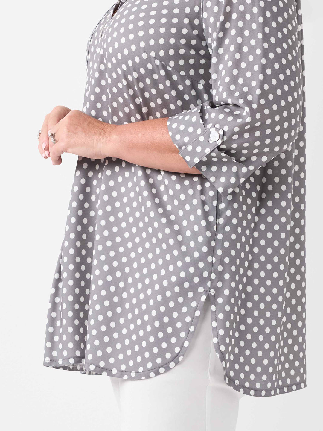A woman wearing a grey and white polka dot blouse with three-quarter tab sleeves and side split