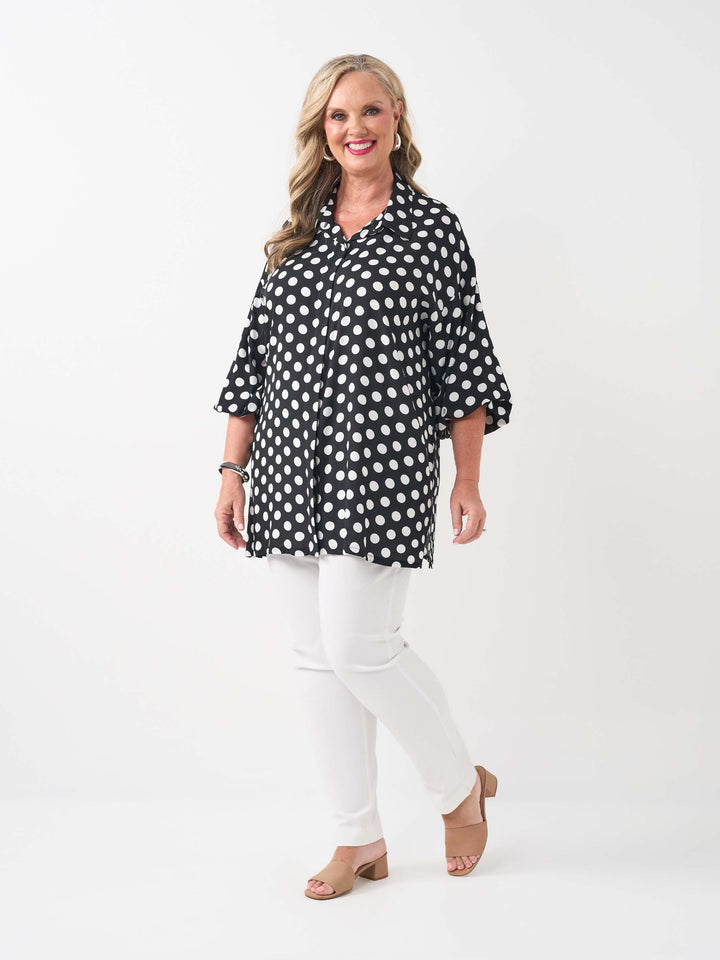 A woman wearing a black collared relaxed fit shirt with a white polka dot pattern, paired with white pants
