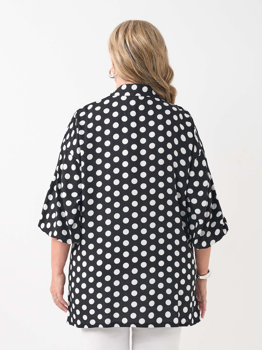 A woman viewed from the back wearing a black collared relaxed fit shirt with a white polka dot pattern, paired with white pants