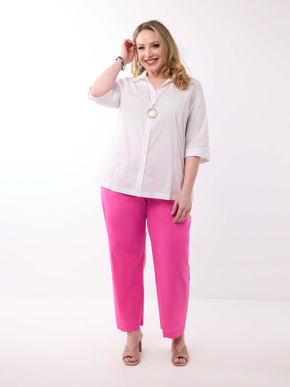 A woman wearing a white button-up shirt with three-quarter tab sleeves and bright pink pants