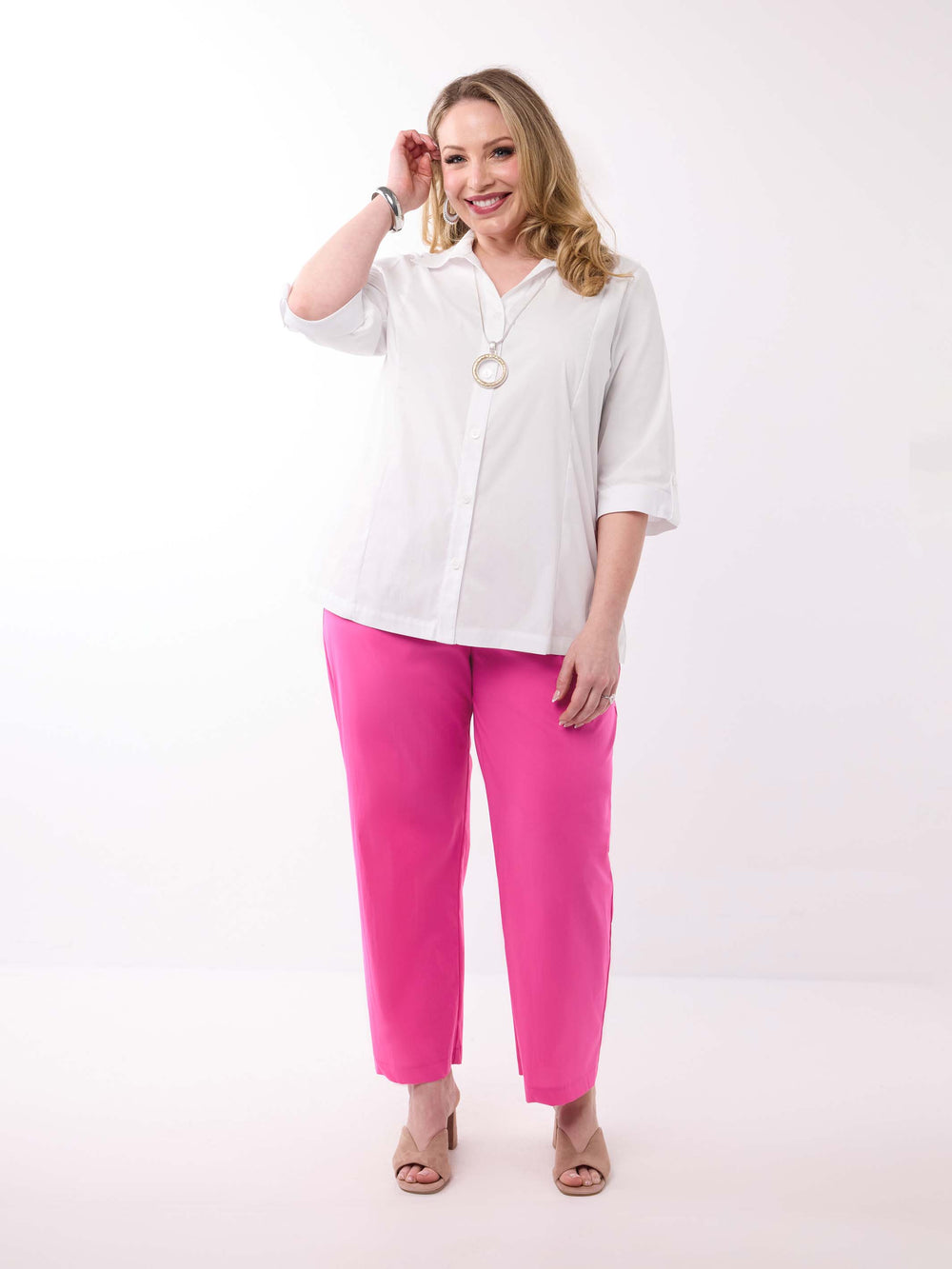 A woman wearing a white button-up shirt with three-quarter tab sleeves and bright pink pants