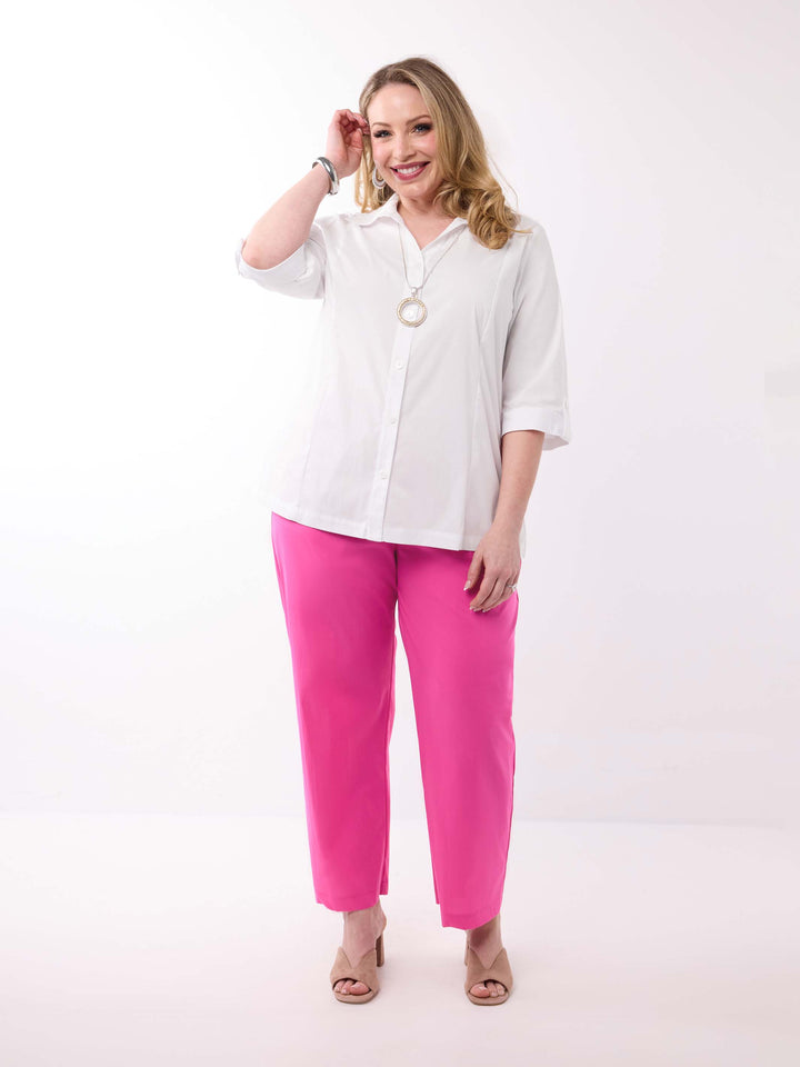 A woman wearing a white button-up shirt with three-quarter tab sleeves and bright pink pants