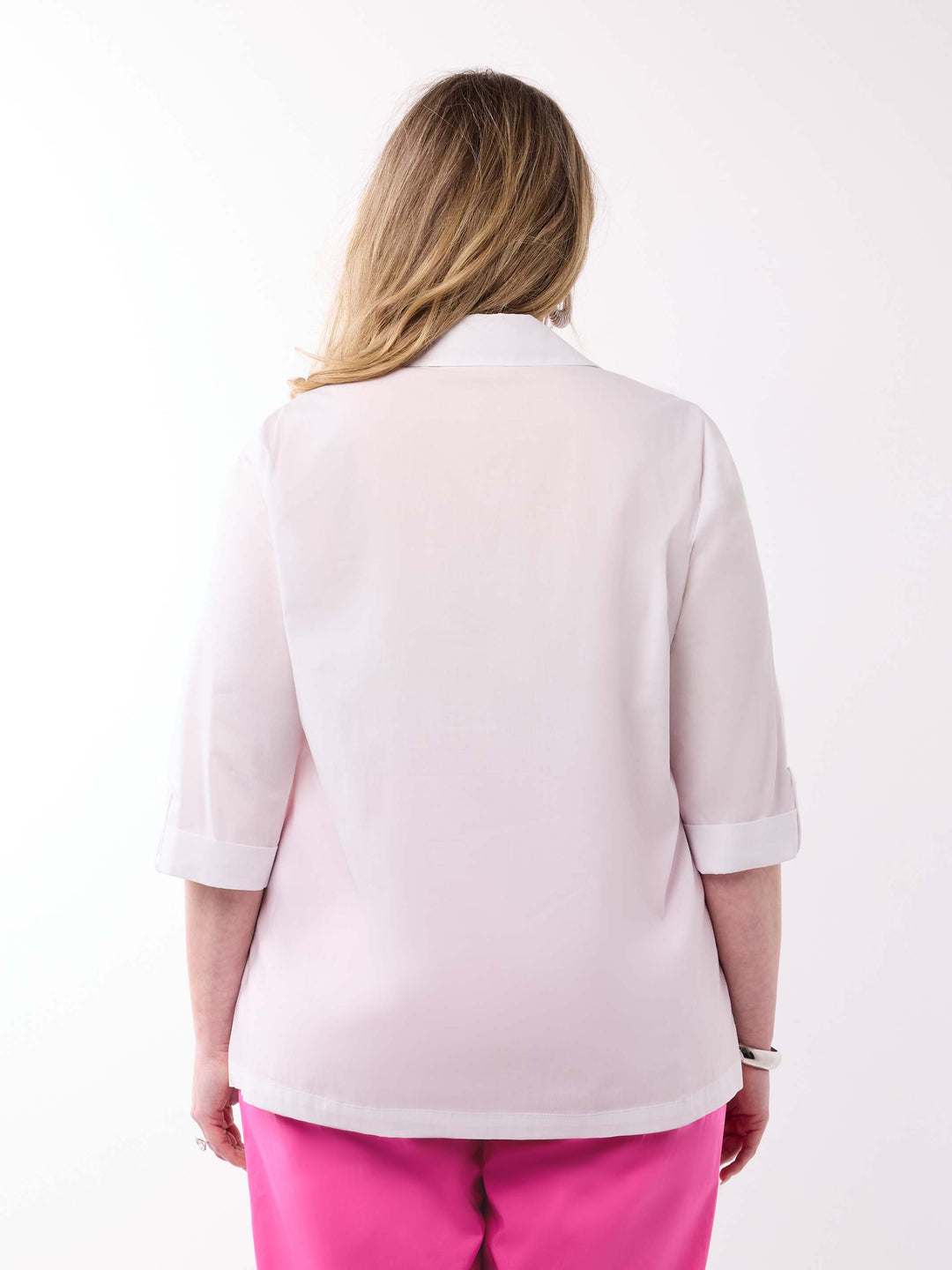 A woman viewed from behind wearing a white shirt with three-quarter tab sleeves and bright pink pants