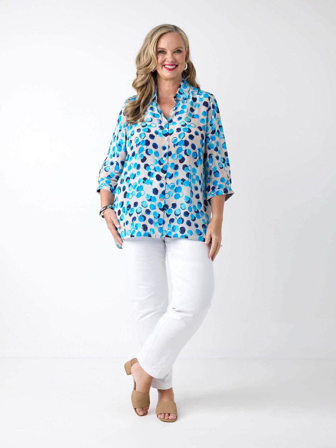 A woman wearing a light white button-up collared shirt with a vibrant blue and navy abstract watercolour dot pattern, paired with white pants