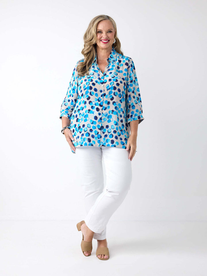 A woman wearing a light white button-up collared shirt with a vibrant blue and navy abstract watercolour dot pattern, paired with white pants