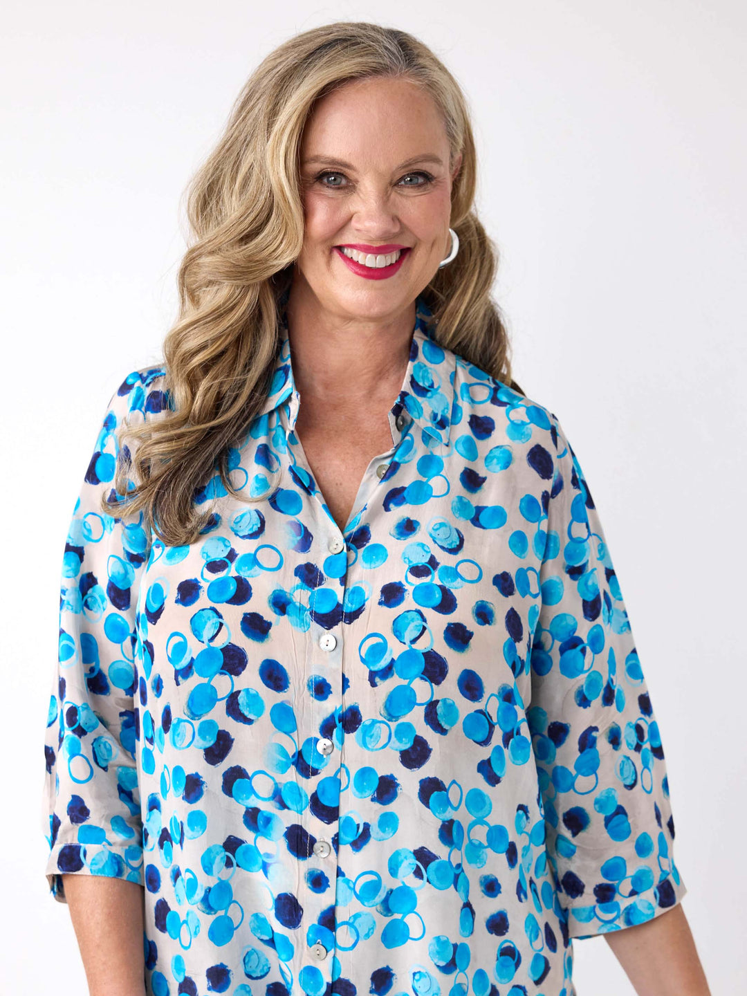 A woman wearing a light white button-up collared shirt with a vibrant blue and navy abstract watercolour dot pattern, paired with white pants
