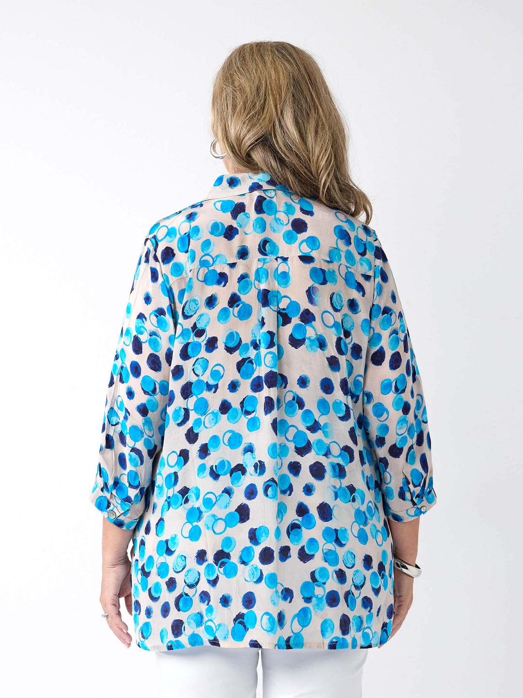 A woman viewed from the back wearing a light white button-up collared shirt with a vibrant blue and navy abstract watercolour dot pattern, paired with white pants