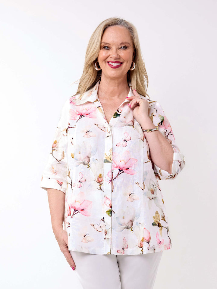 A woman wearing a collared linen shirt with pink magnolia floral print on white, paired with a pair of white pant