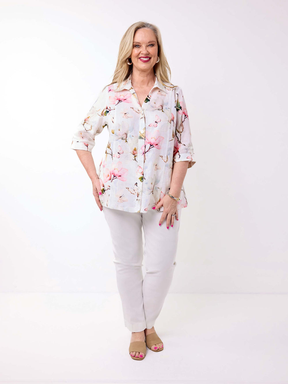 A woman wearing a collared linen shirt with pink magnolia floral print on white, paired with a pair of white pant