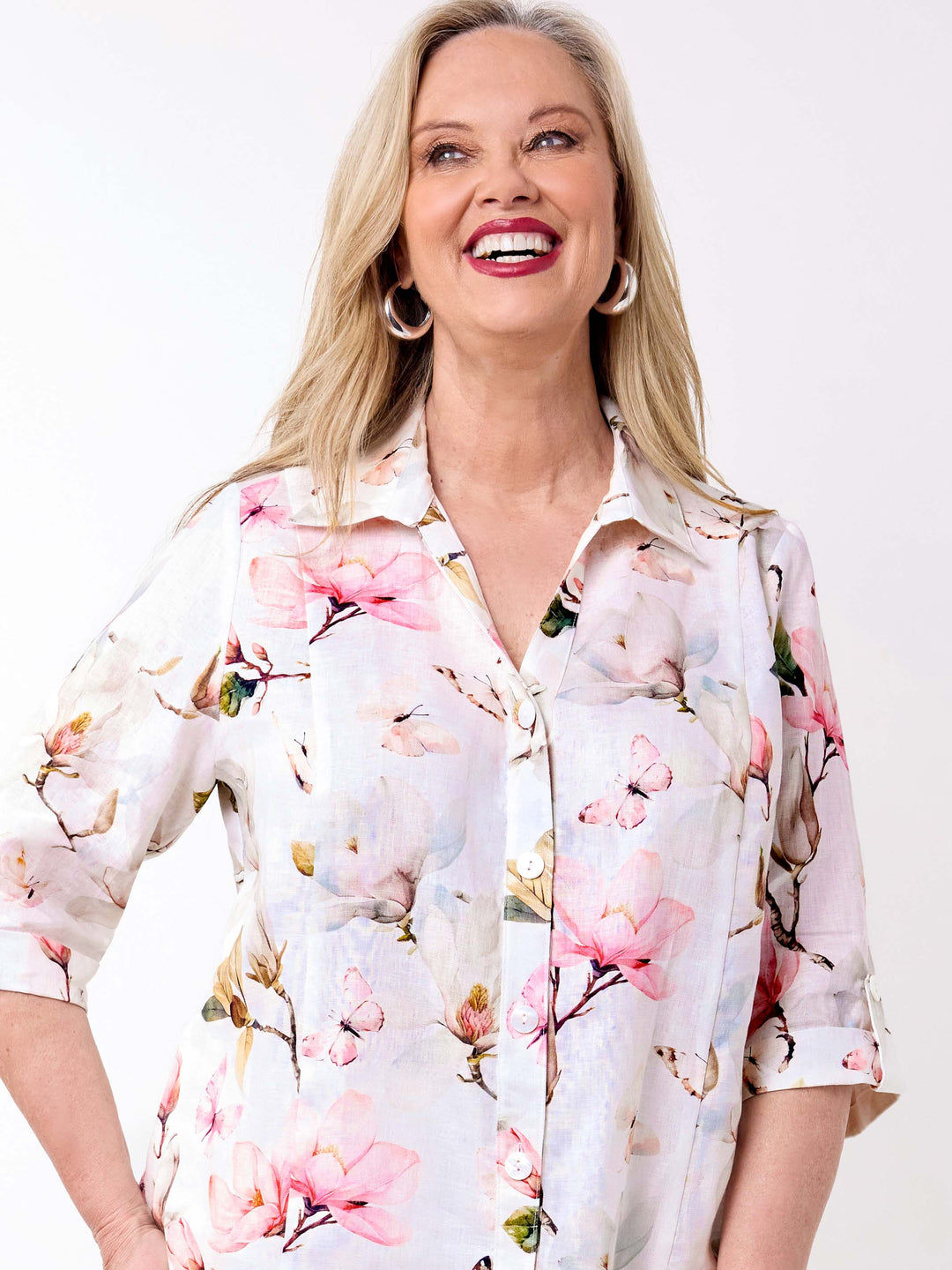 A woman wearing a collared linen shirt with pink magnolia floral print on white, paired with a pair of white pant
