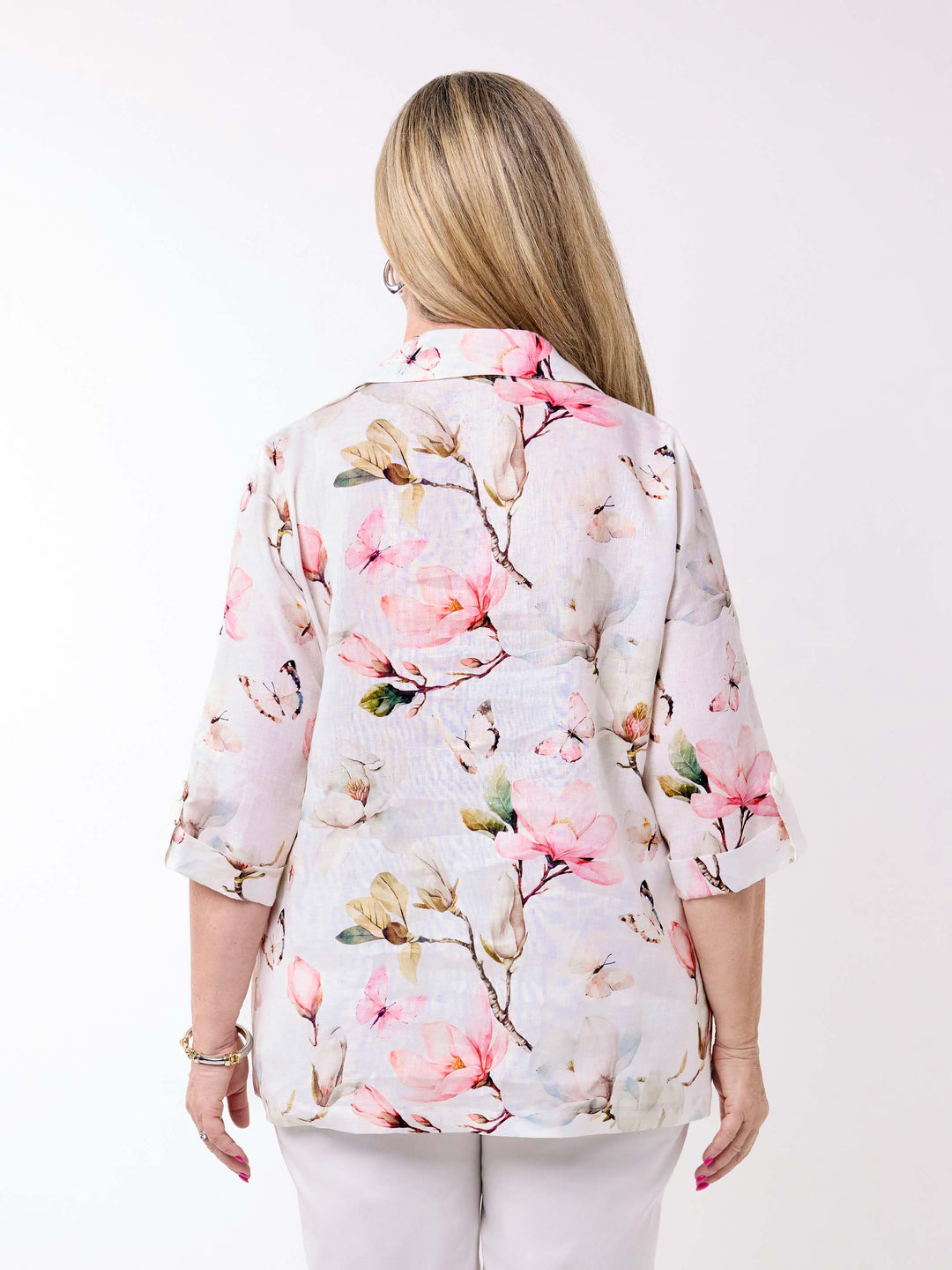 A woman wearing a collared linen shirt with pink magnolia floral print on white, paired with a pair of white pant
