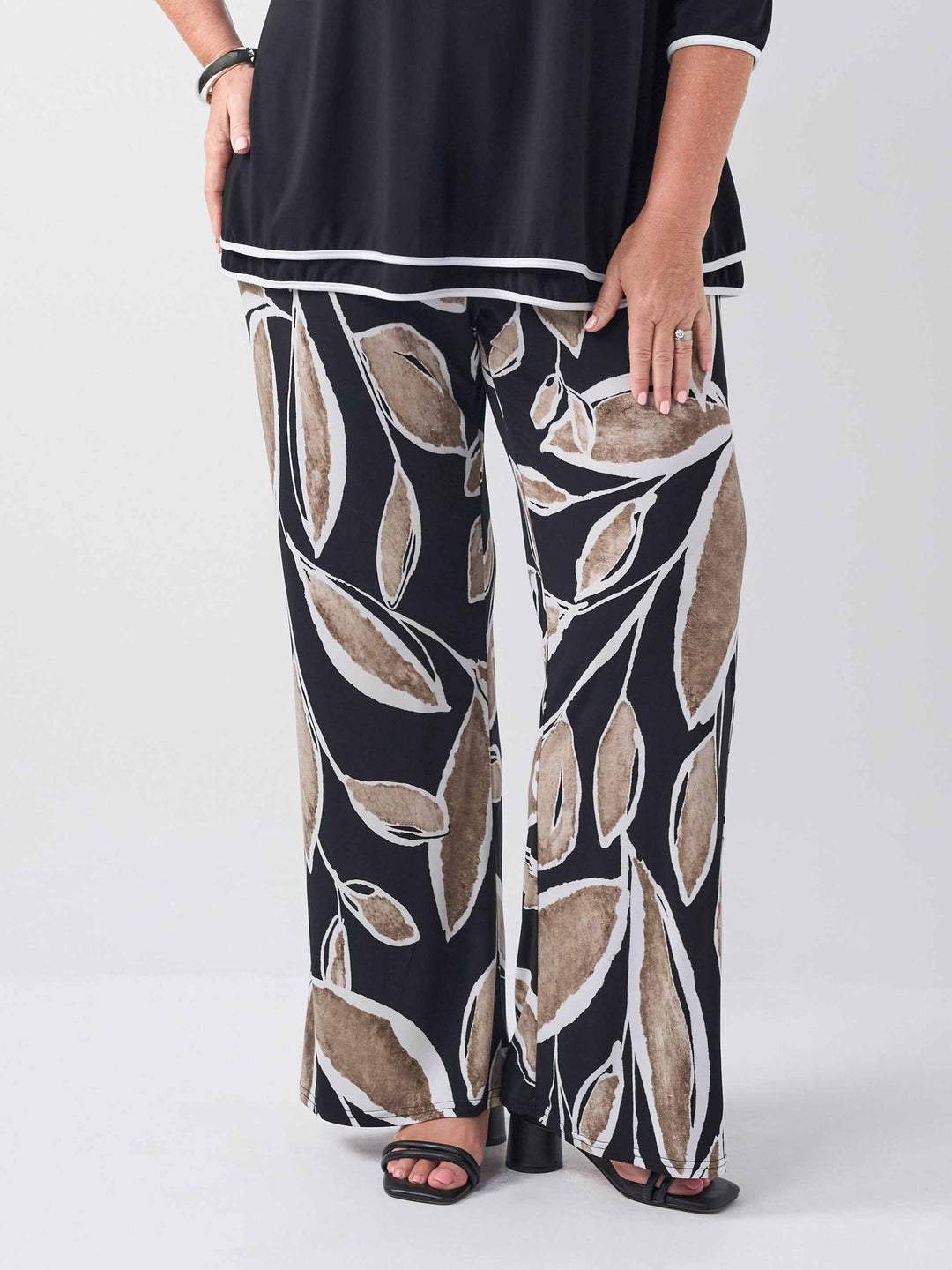 front view of a wide-leg palazzo pants with a black base and an abstract leaf pattern in beige and white