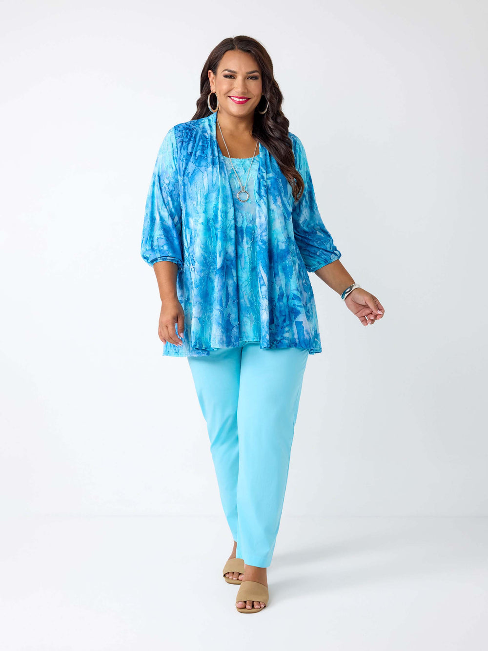 A woman wearing a two-piece outfit consisting of a blue tie-dye burnout cami and jacket set, paired with light blue pant