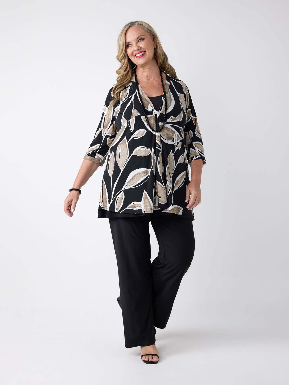 woman wearing a black three-quarter sleeve lightweight jacket with a beige and white leaf pattern and one button closure, paired with classic black jersey palazzo pant