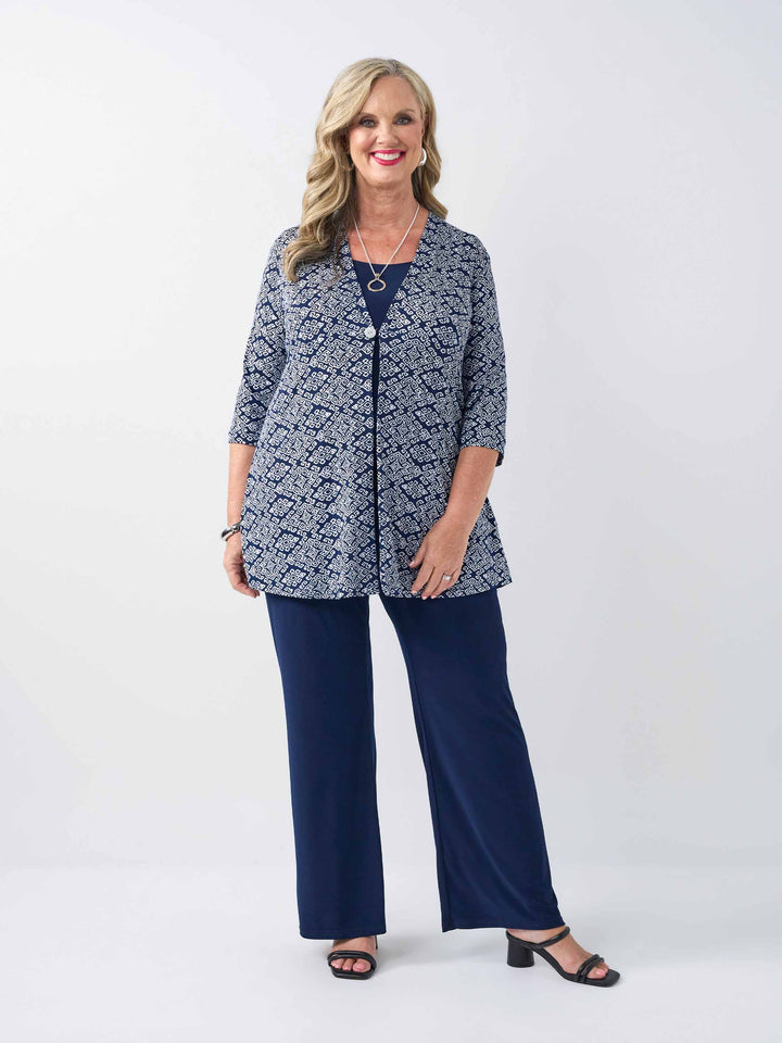 woman models a navy blue and white geometric patterned lightweight jacket with three-quarter sleeves and a button placket, paired with navy palazzo pants 