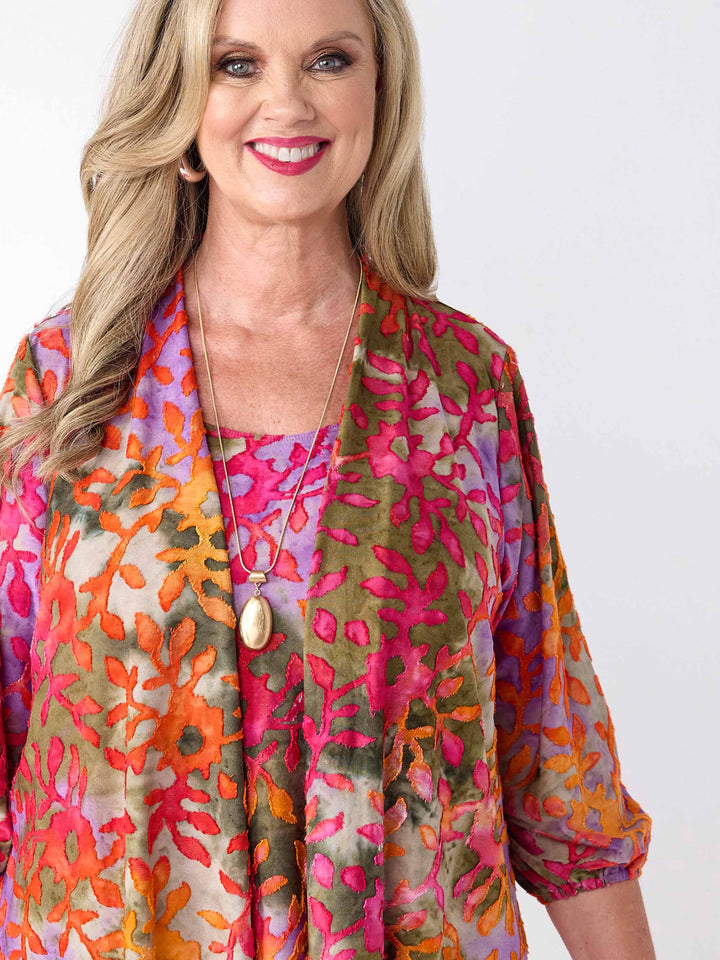 A detailed view of a woman wearing a colourful burnout jacket with three-quarter sleeves in pink over a matching cami and bright pink pants