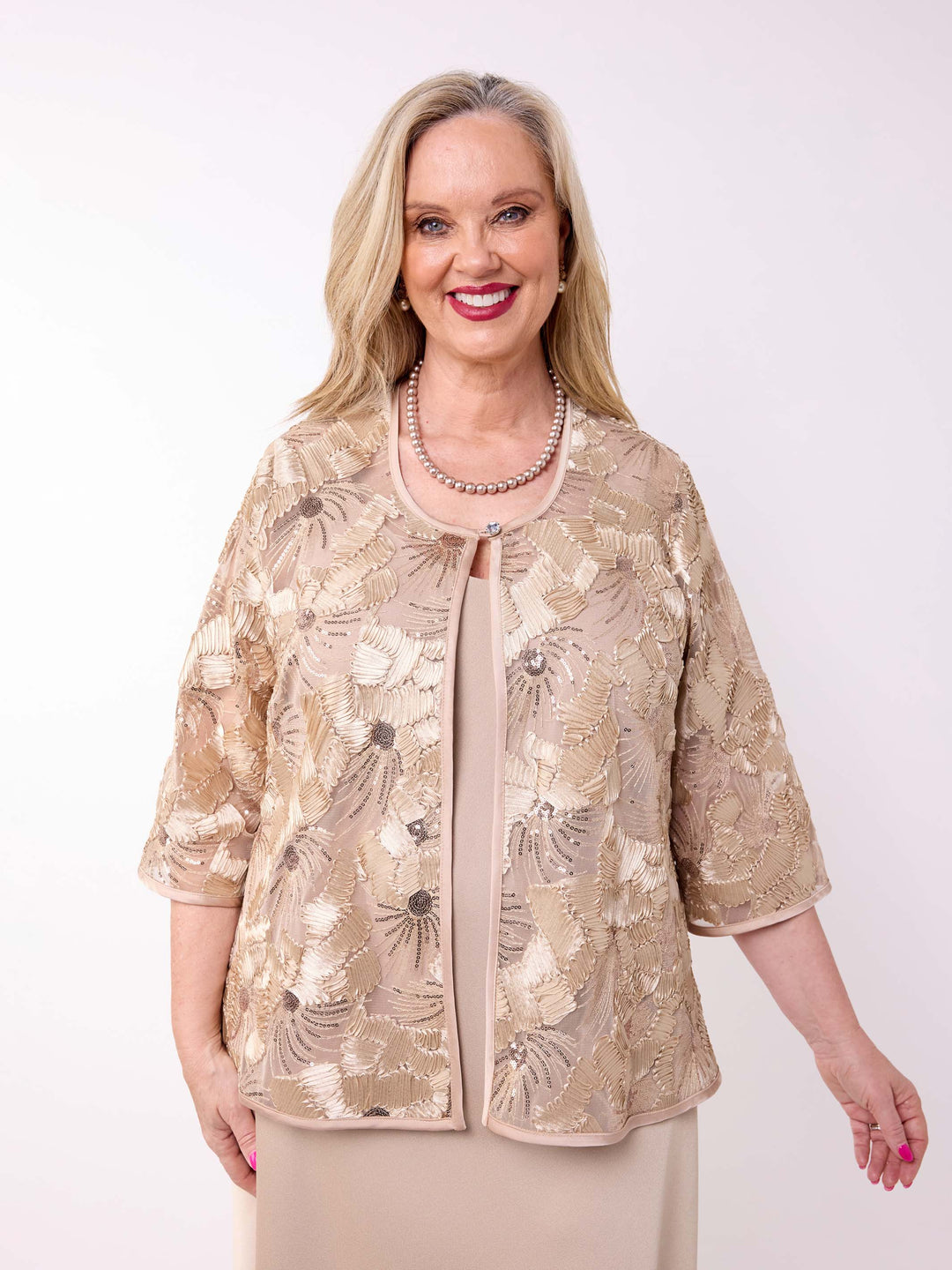 A woman wearing a champagne gold floral embroidered jacket over a matching champagne evening dress
