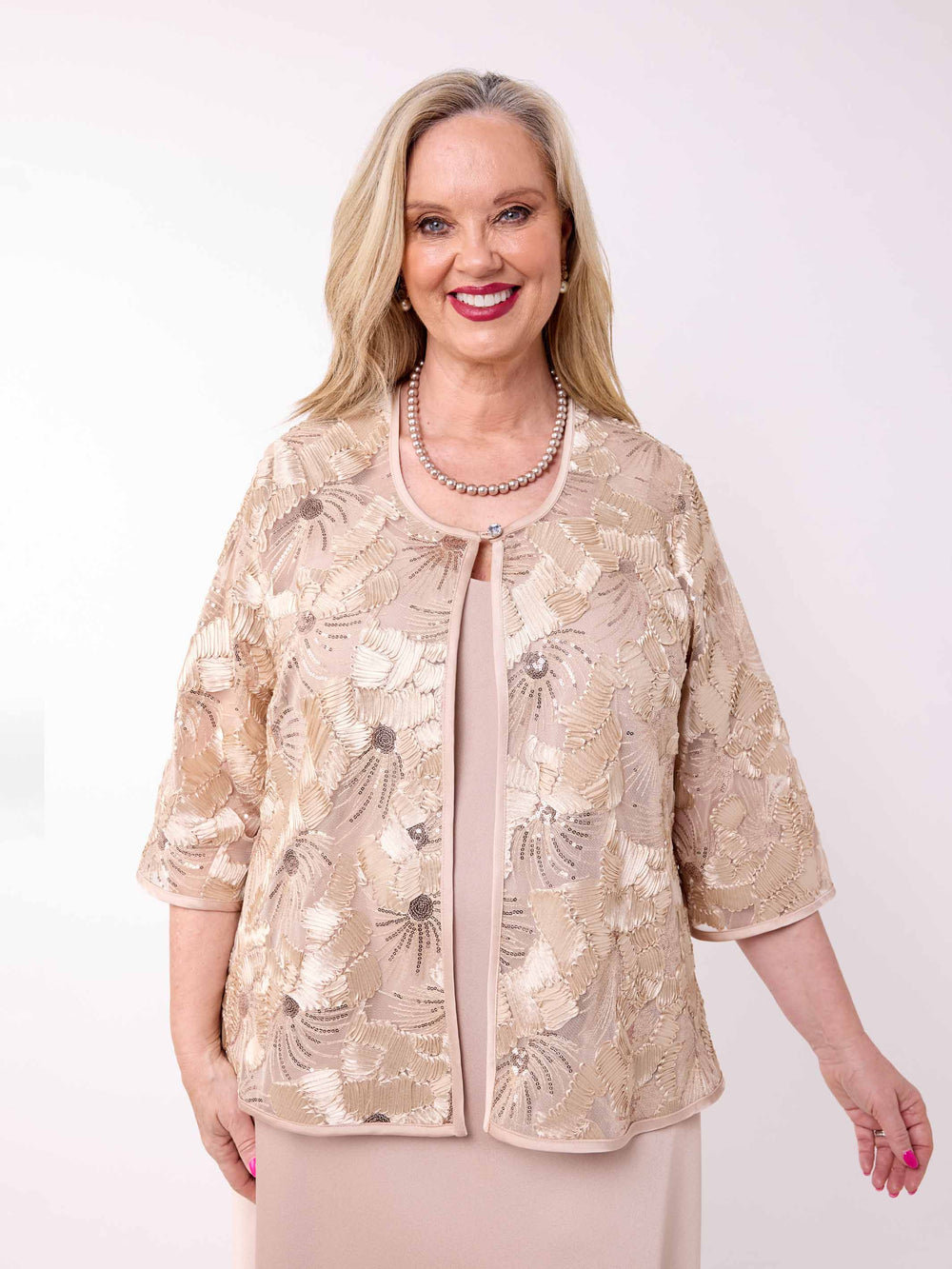 A woman wearing a champagne gold floral embroidered jacket over a matching champagne evening dress