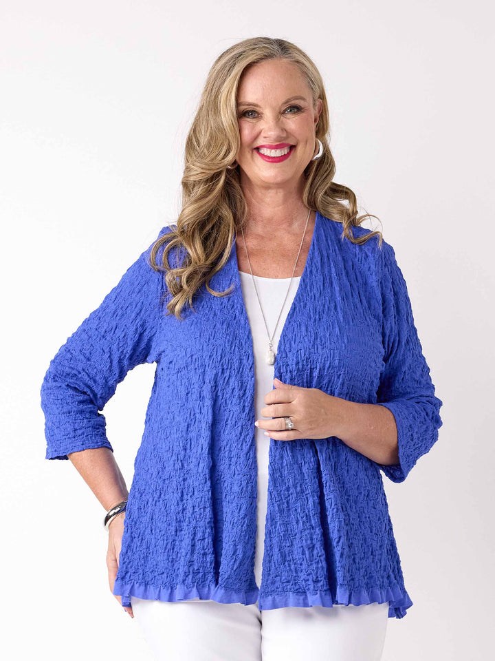 A woman wearing a textured royal blue open-front cardigan over a white top and white pants