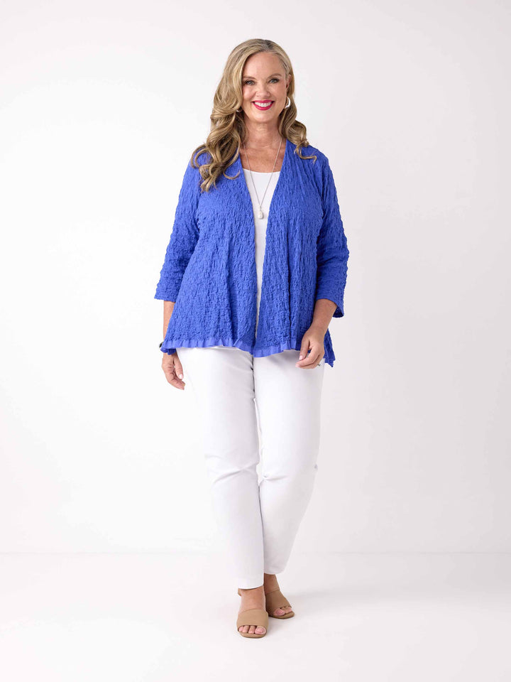 A woman wearing a textured royal blue open-front cardigan over a white top and white pants
