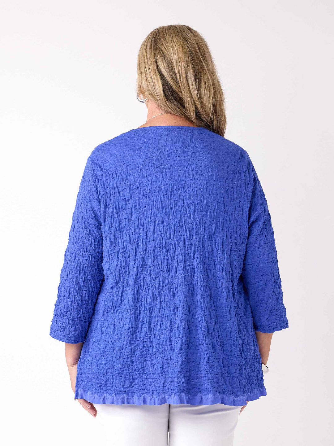 A woman wearing a textured royal blue open-front cardigan over a white top and white pants
