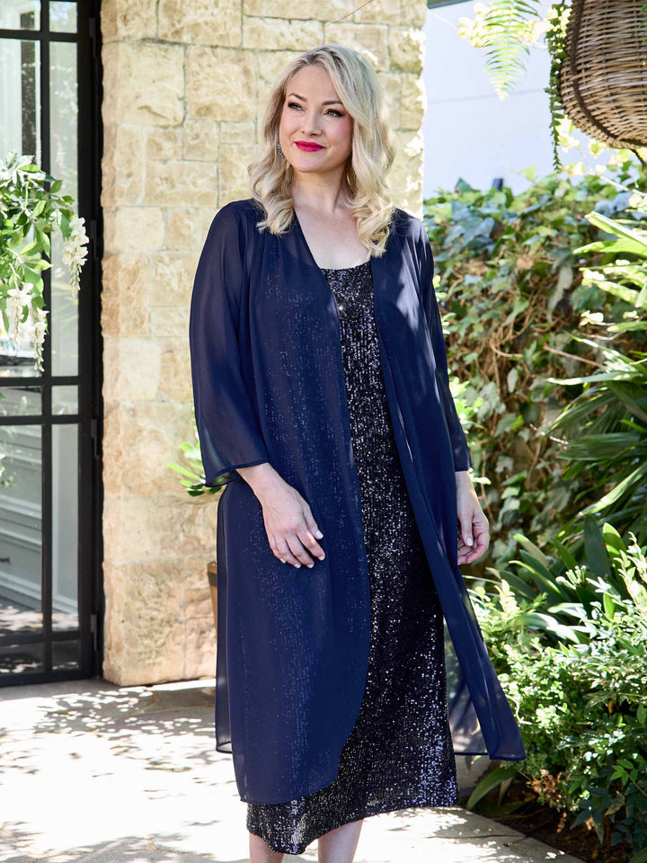 A woman wearing a navy sheer evening long jacket styled with a navy sequin evening dress