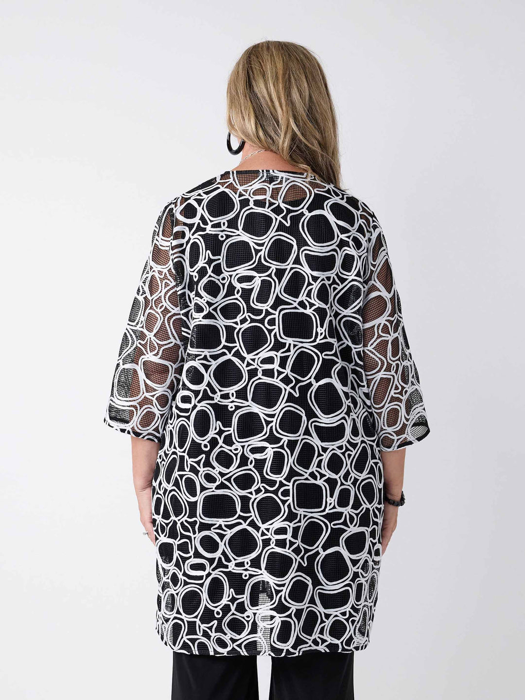 A woman wearing a black and white abstract patterned open-front evening longline jacket over a black top