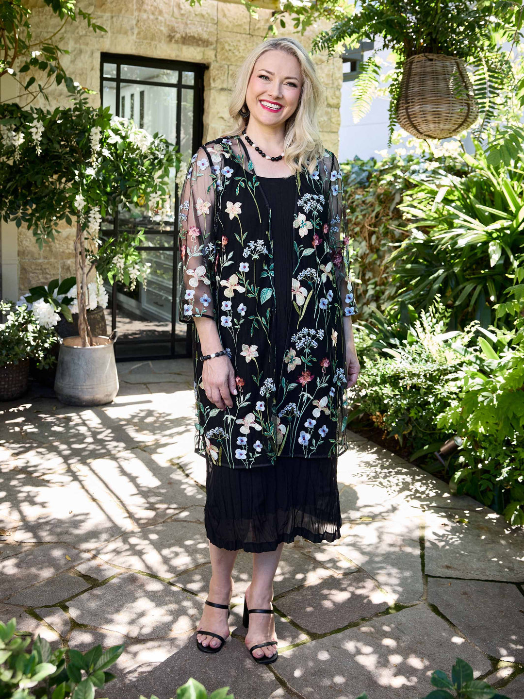 A woman wearing a sheer black embroidered evening jacket over a black crushed dress