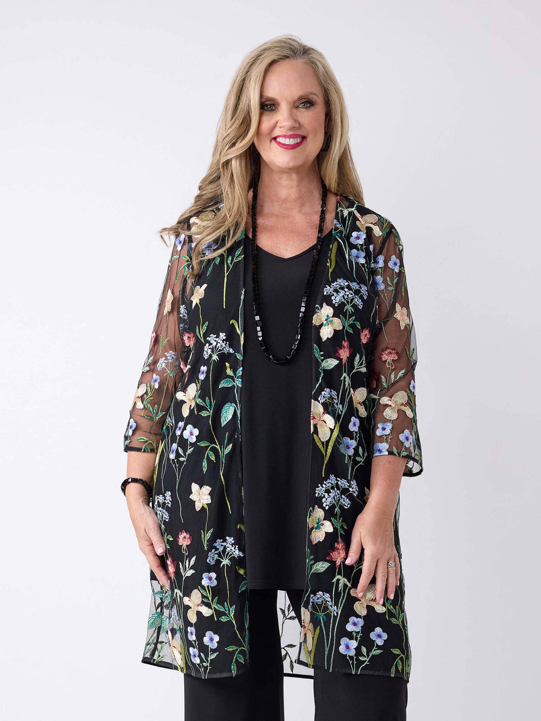 A woman wearing a sheer black embroidered evening jacket over a black cami and palazzo pant