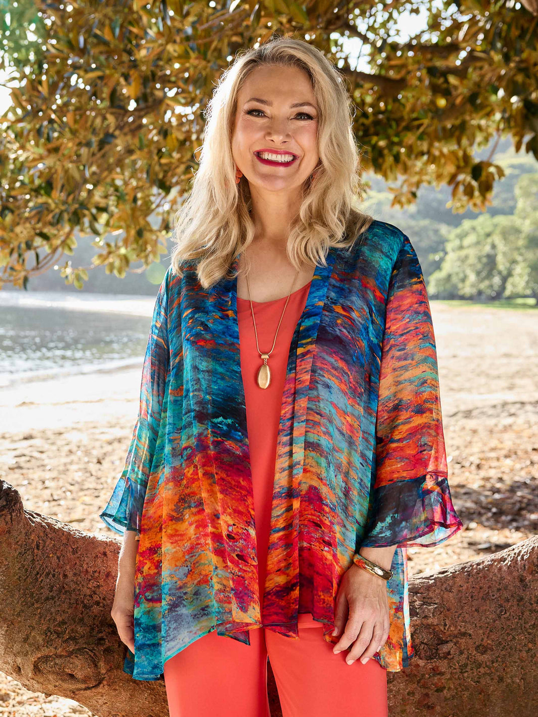 A woman wearing a colourful abstract-print frill sleeves georgette jacket over a coral-orange cami and matching coral pants.