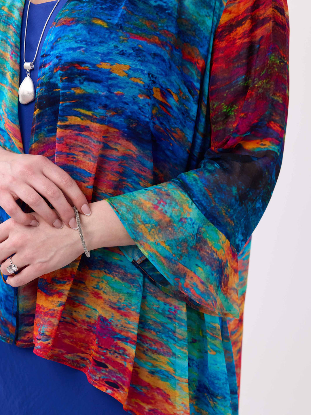 A close-up of a woman wearing a vibrant, multicoloured abstract print georgette jacket with blue, red, orange, and yellow tones