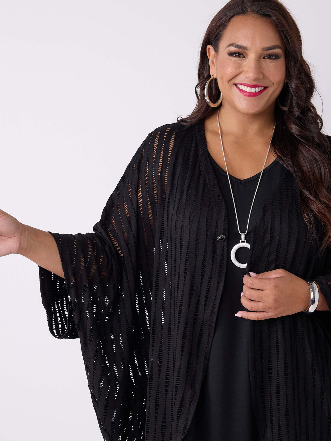 A close-up view of a woman wearing a black drapery longline evening jacket with ladder lace detail, styled with a black v-neck swing cami 