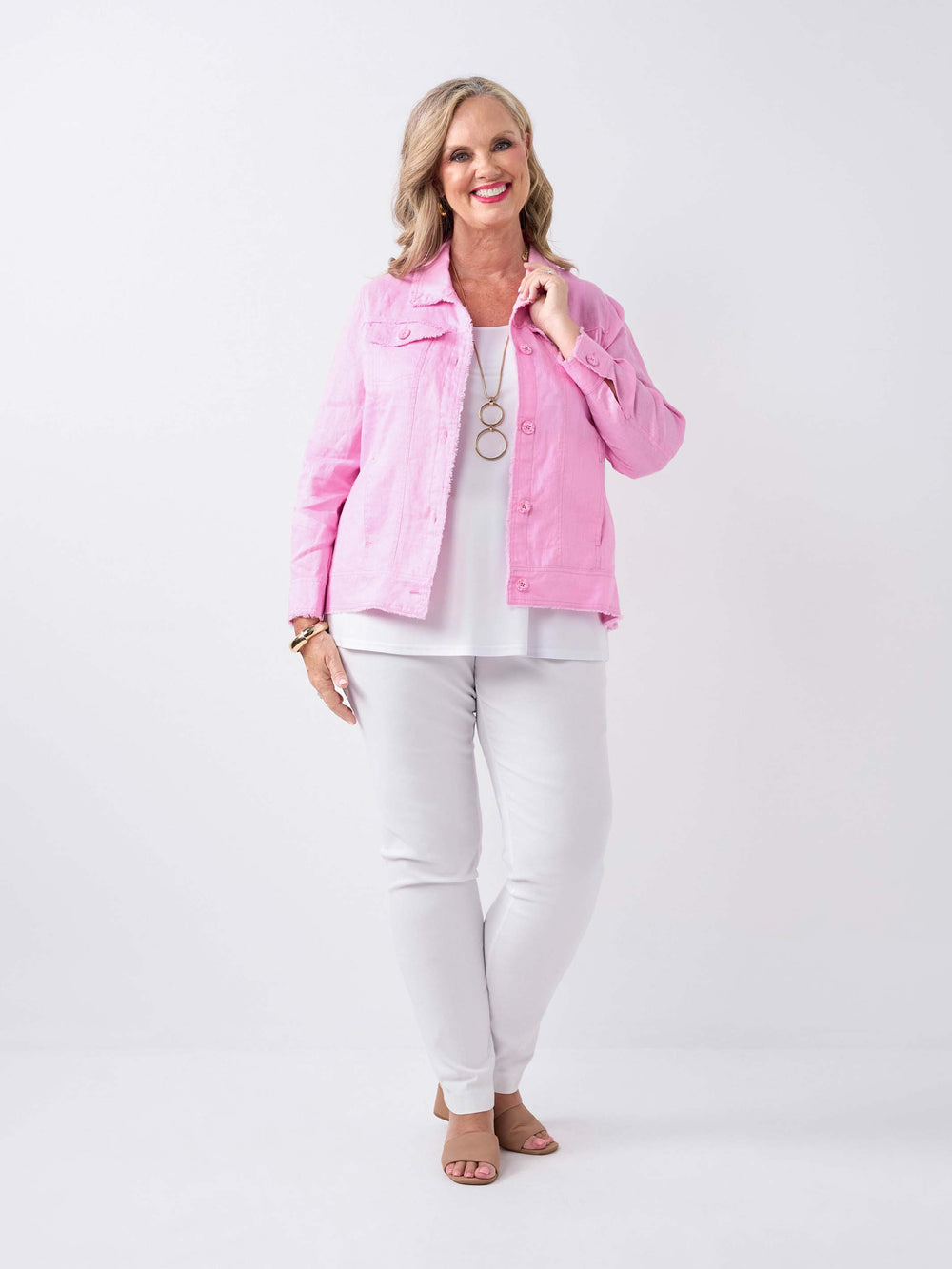 A woman wearing a lightweight pale pink linen jacket over a white top and white pants